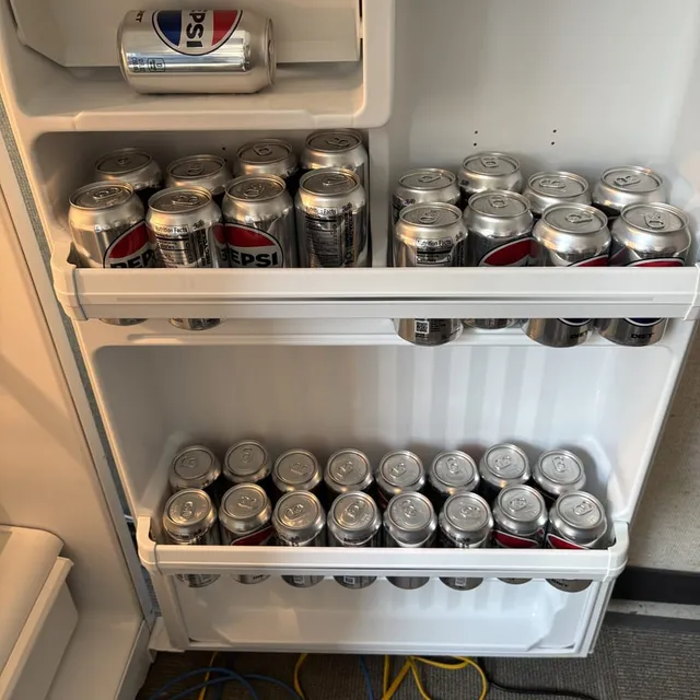 A small lab fridge with its door open, every shelf packed with cans of Diet Pepsi